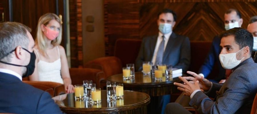 Armando Armas conversando con participantes de una reunión, sentados alrededor de mesas en un salón.