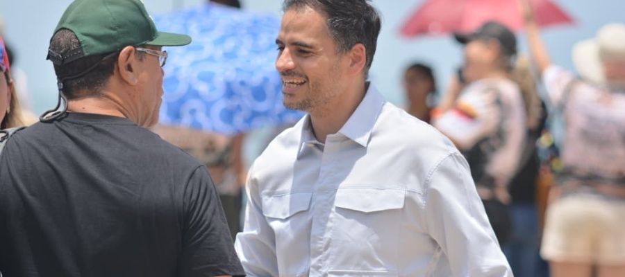 Armando Armas con camisa clara conversando con un hombre que lleva gorra verde y camiseta negra.