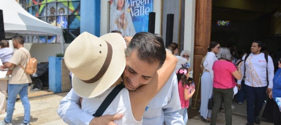 Armando Armas abrazando a una persona con sombrero en las inmediaciones de un edificio religioso.